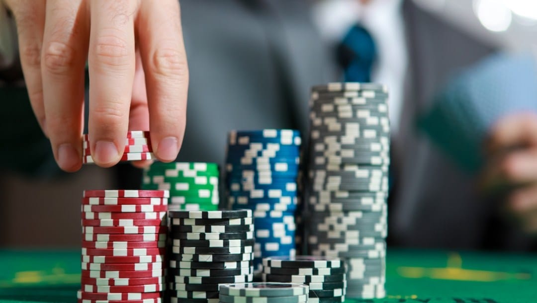 Stacks of poker chips of different values, on the left a hand picks red chips from a stack