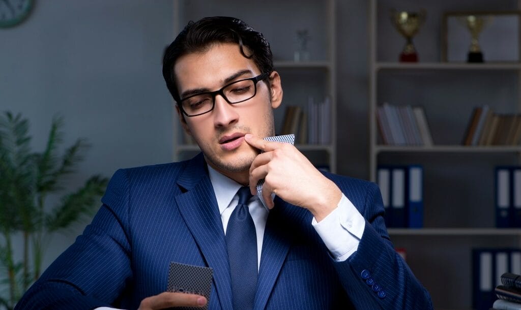A man in a suit and glasses ponders over a game of poker