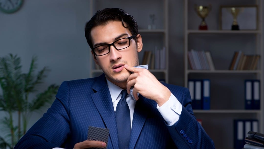 A man in a suit and glasses ponders over a game of poker