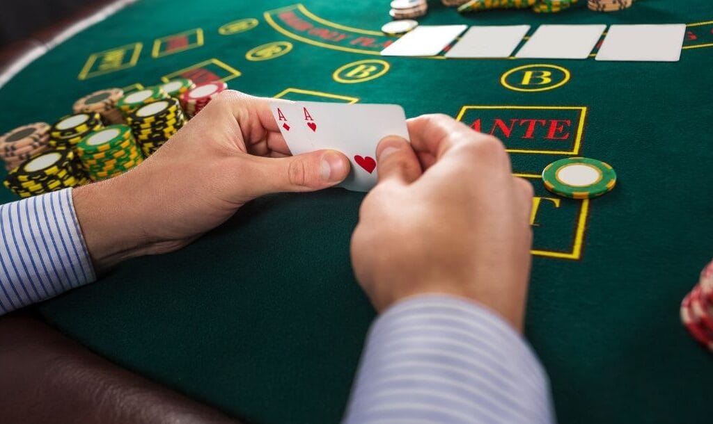 A person sitting at a Texas Hold’em table, holding an Ace of Hearts, and an Ace of Diamond, with poker chips stacked on the table.