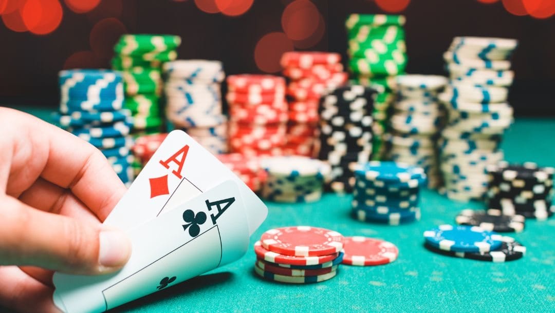 A person revealing an Ace of Diamonds, and an Ace of Clubs, at a poker table, with casino chips stacked on the table.
