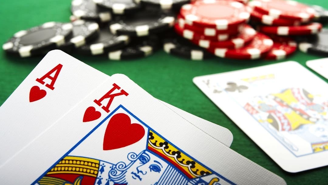 A close up of an Ace of Hearts, and a King of Hearts, at a poker table, with poker chips and other playing cards arranged on a poker table.