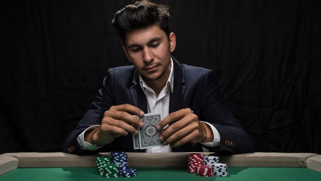 a man looking at his two hole cards in his hands while sitting at a poker table
