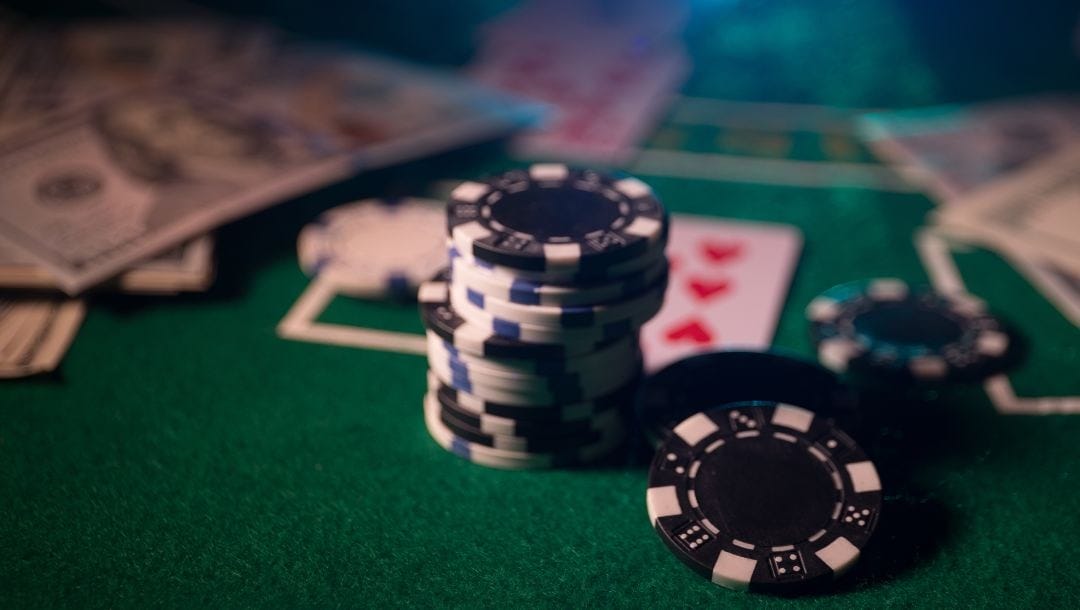 poker chips on a green felt poker table with playing cards and money bills blurred in the background