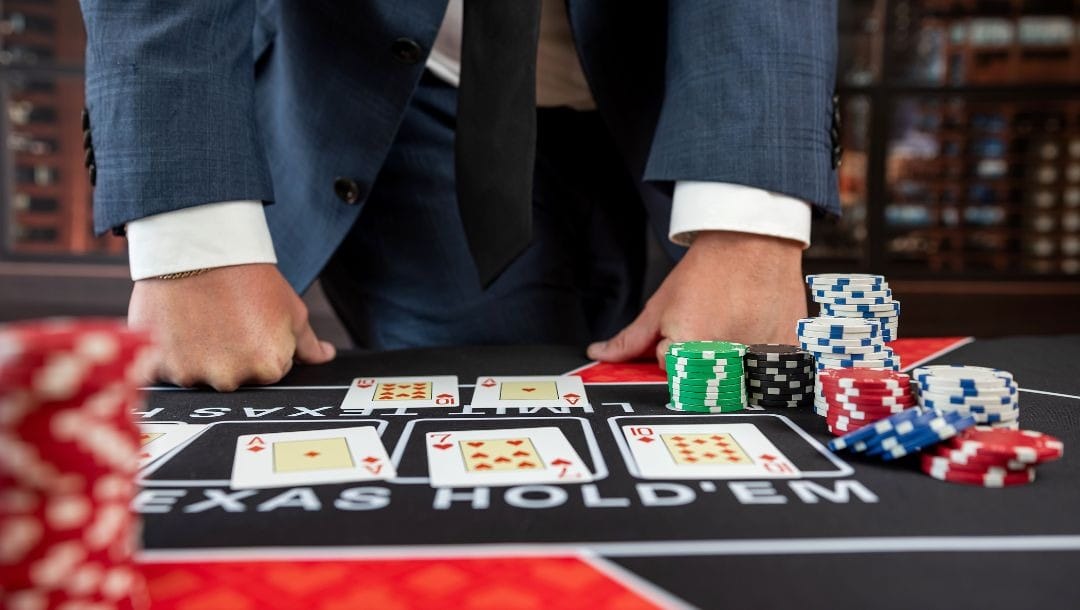 A person standing in front of a poker table, with playing cards, and poker chips arranged in front of him, on top of the poker table.