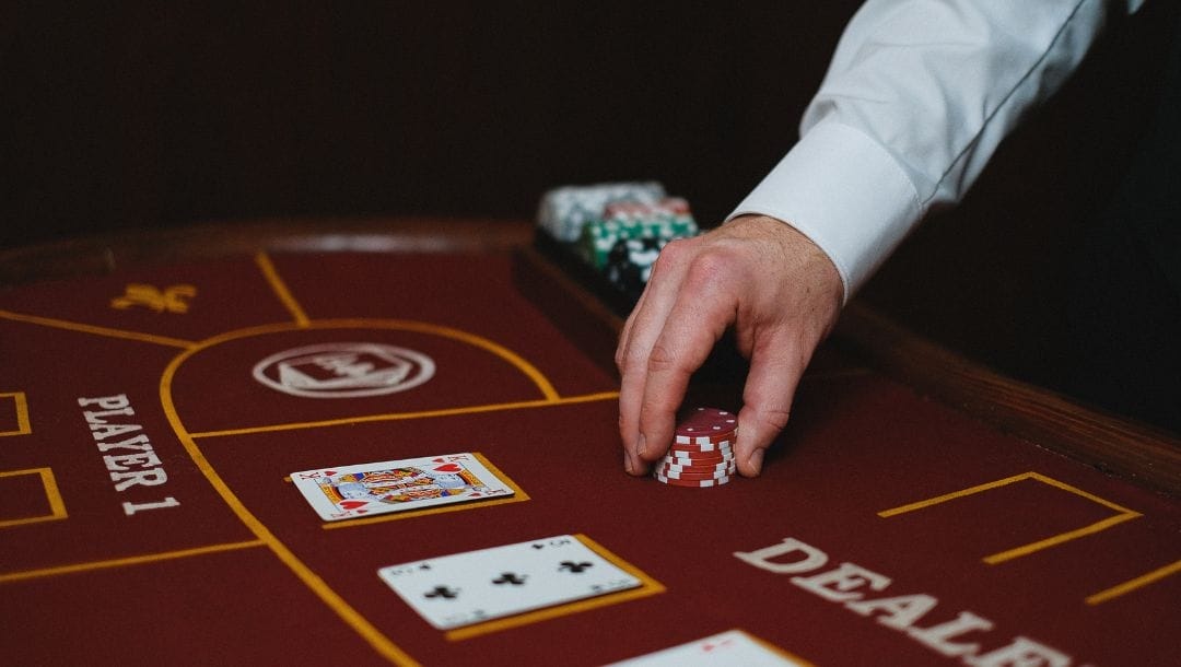 A croupier placing a stack of poker chips on a red felt table.