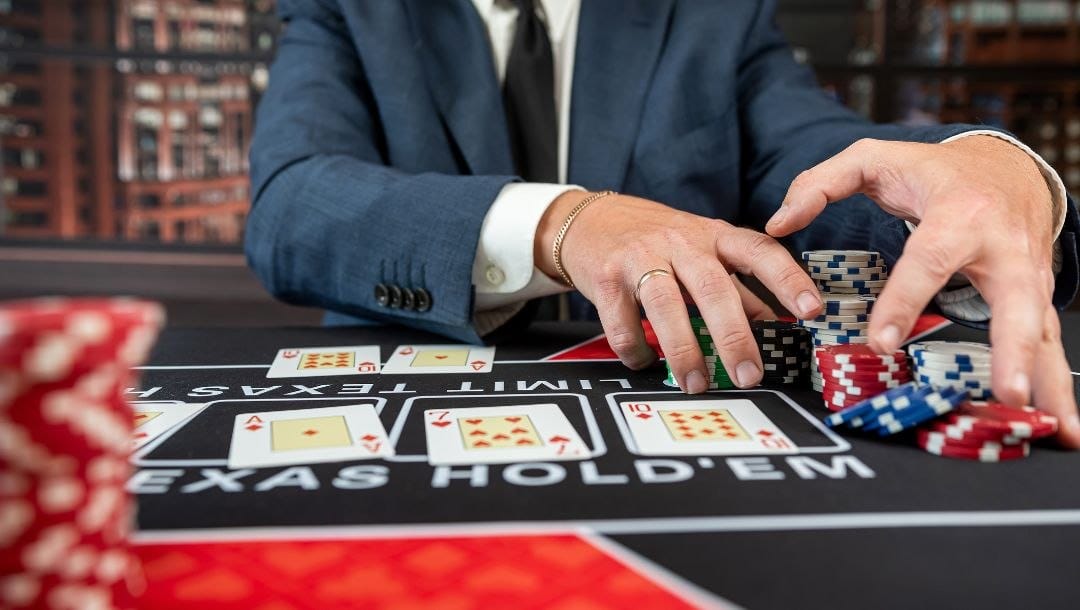 a man pulls stacks of poker chips towards him on a poker table with playing cards on it