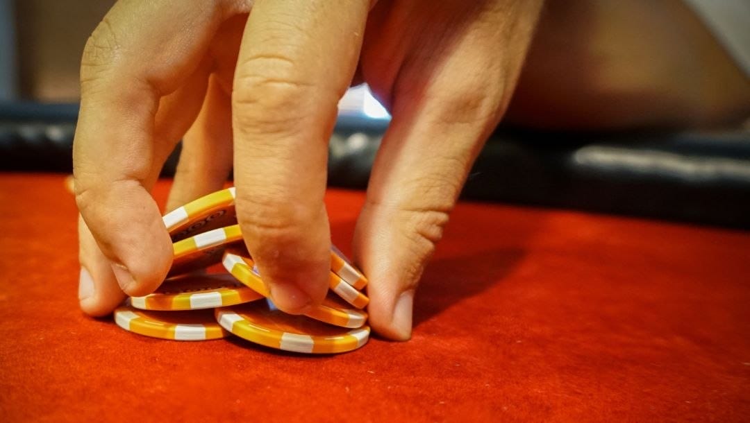 close up of a man’s hands shuffling poker chips on a red poker table