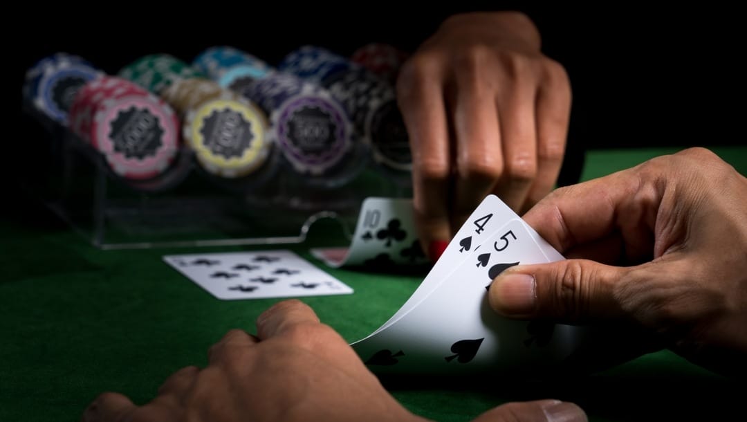 A hand holds playing cards on poker table and with stacked chips in background