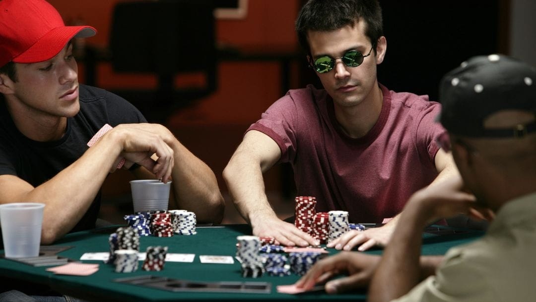 Three people around a green felt poker table with stacks of poker chips in front of them.
