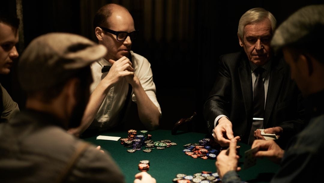 Five people around a green felt poker table with poker chips scattered around.