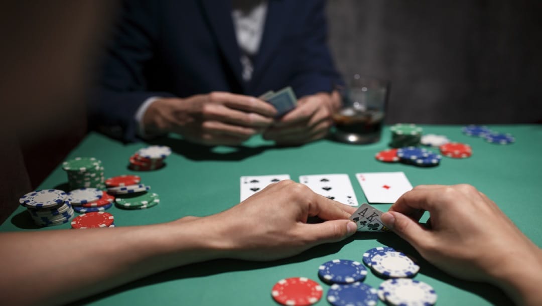 A player is checking their cards discreetly, keeping them close to the green felt table that has many poker chips spread across.