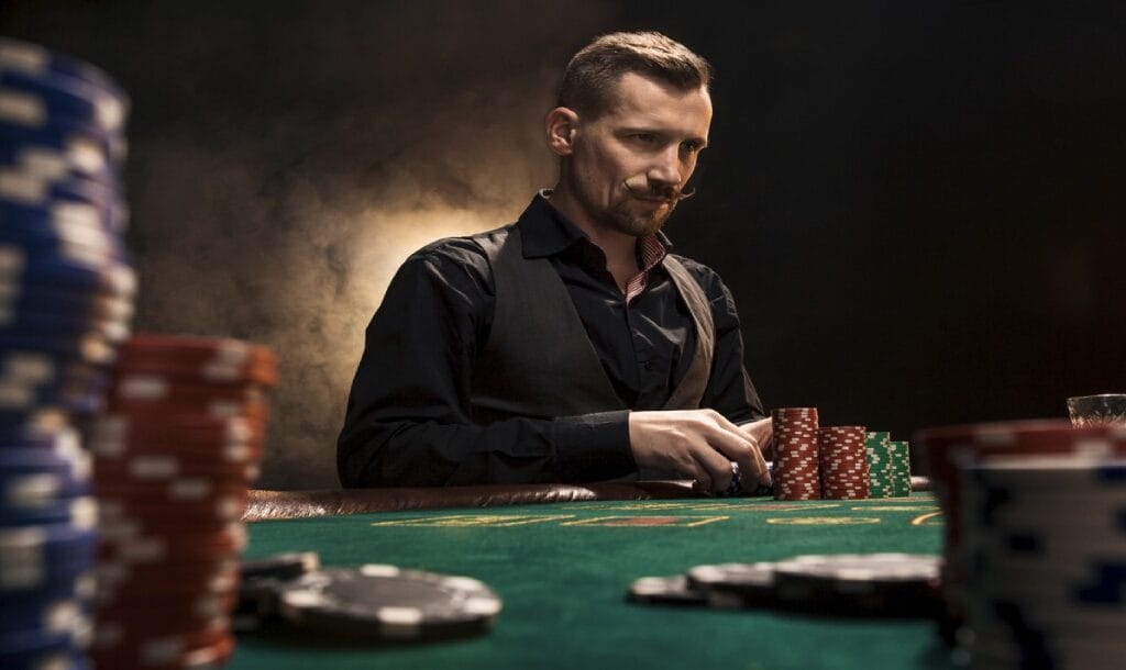 A man sitting at a poker table is surrounded by poker chips, and is thinking about his next move while holding his poker chips.