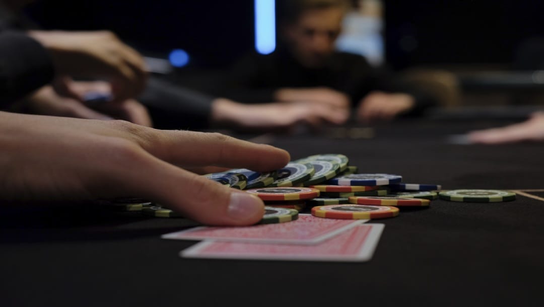 A hand is pushing forward some poker chips that are on top of two playing cards.