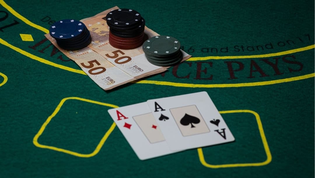An ace of Spades, and an ace of Diamonds ,money, and poker chips, arranged on a poker table.
