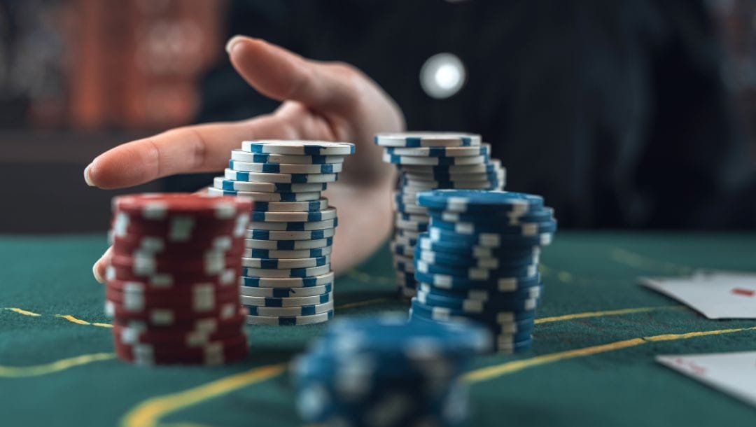 a hand pushes stacks of poker chips forward on a poker table with playing cards on it