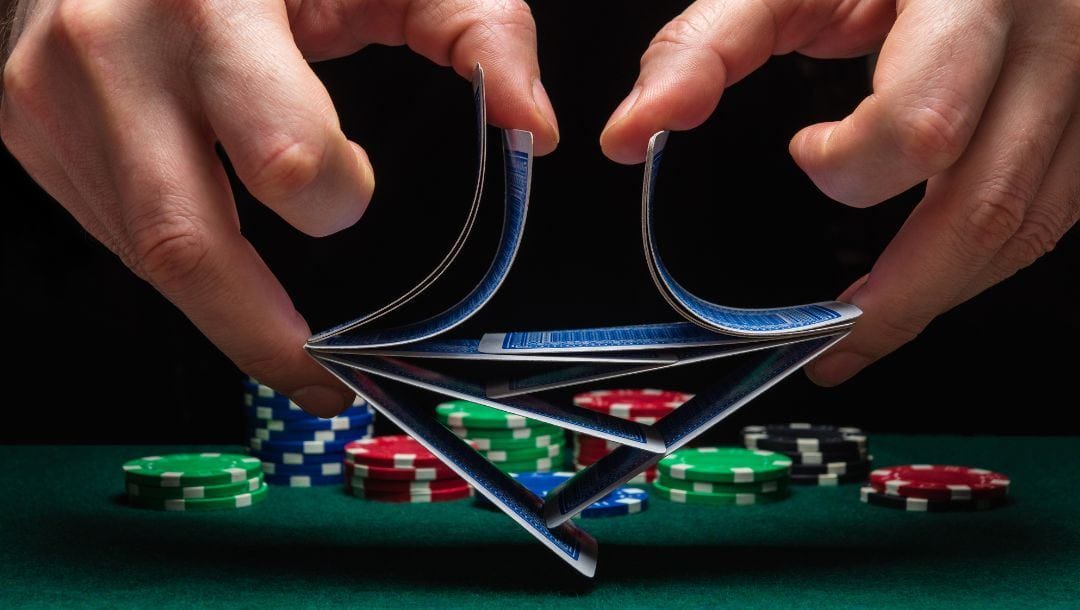 close up of a person shuffling playing cards above a green felt poker table with poker chips on it