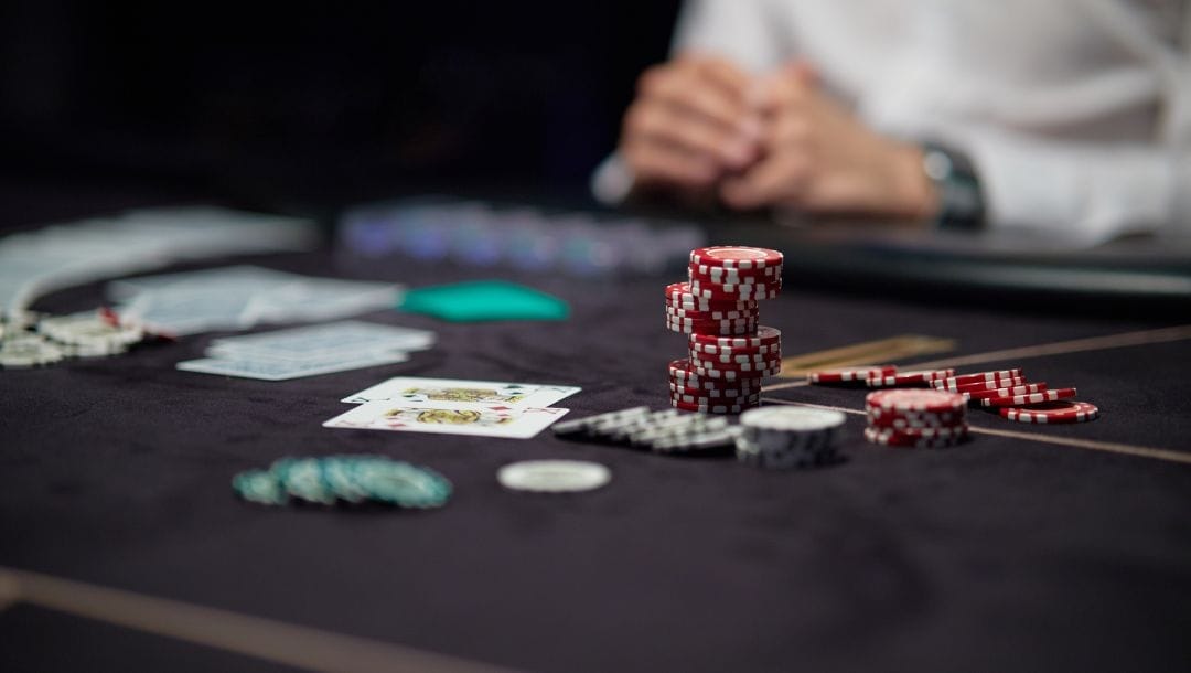 poker chips and playing cards on a black poker table, a person is sitting at the table blurred in the background