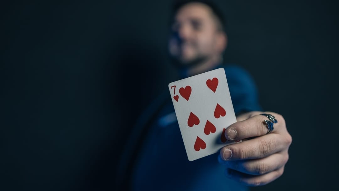 A man holds up a seven of hearts