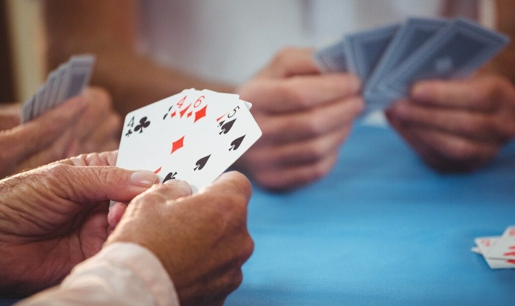Three pairs of hands hold playing cards on a blue table