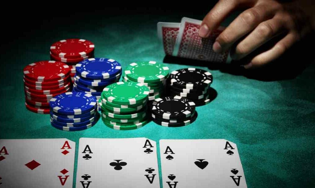 Three aces and chips on a poker table with a player’s hand in the background