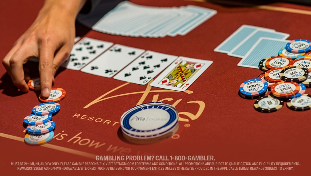 A player at a red poker table, focused on their cards and a stack of chips.