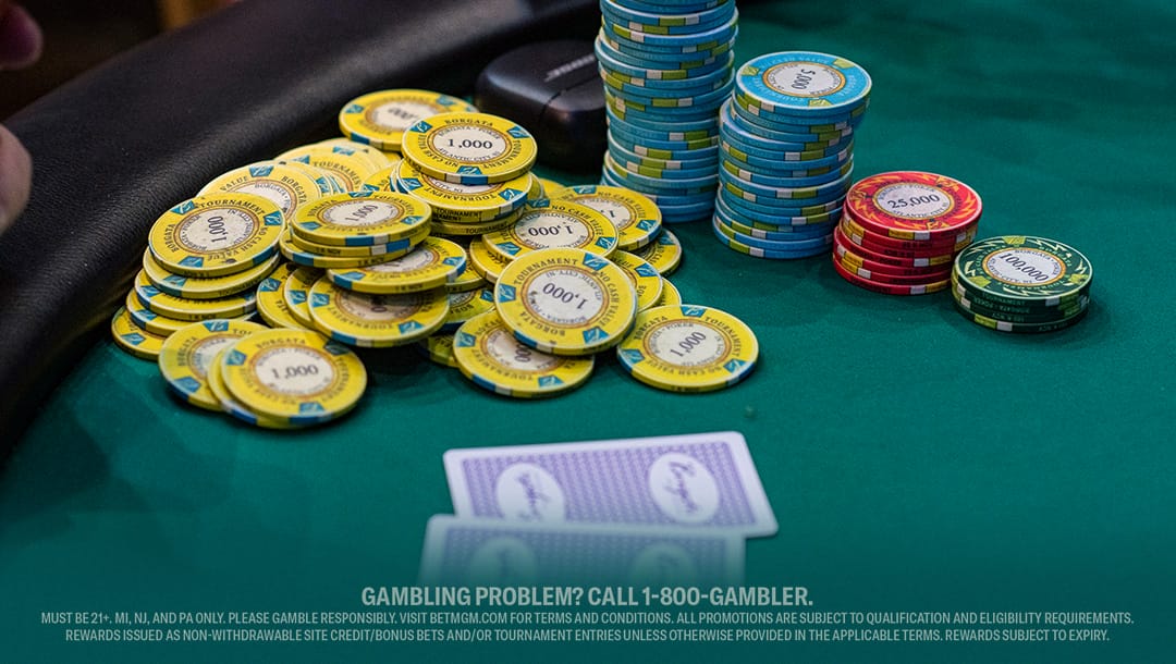 A poker player sits at a table surrounded by stacks of colorful chips, ready for the next hand.