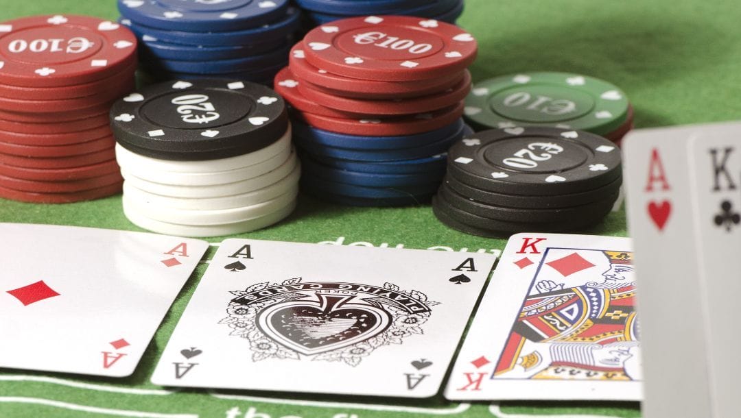 Ace of Diamonds, Ace of Spades, and King of Diamonds lying face up. Ace of Hearts and King of Clubs are being held up. Stacks of poker chips in the background.