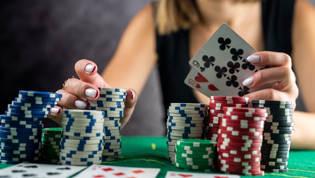 Person’s hand taking poker chips from pile at round poker table