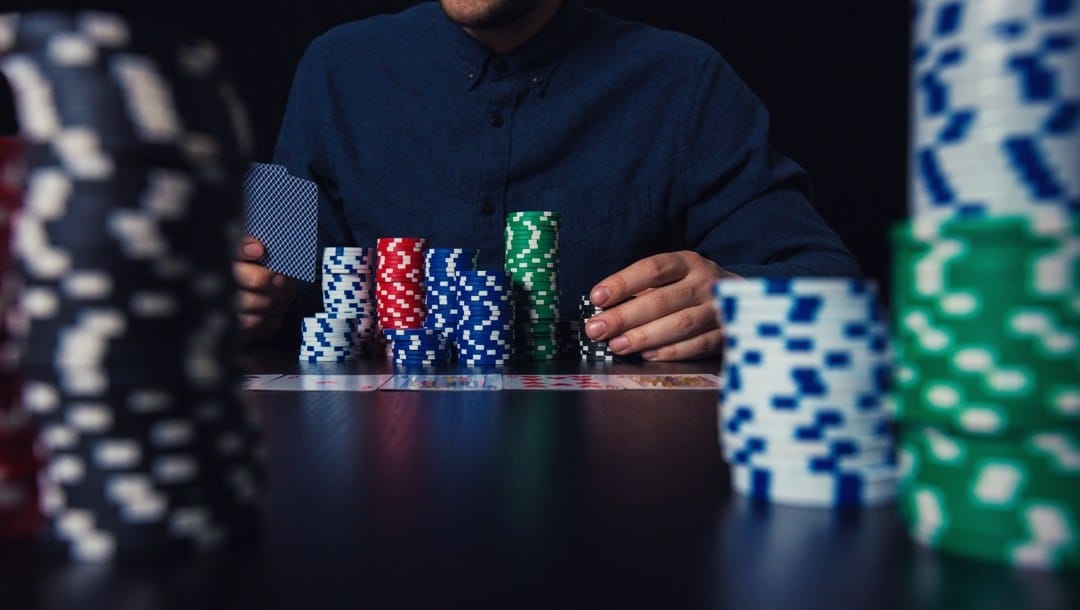 Close-up of poker player holding cards and betting chips at the casino table.