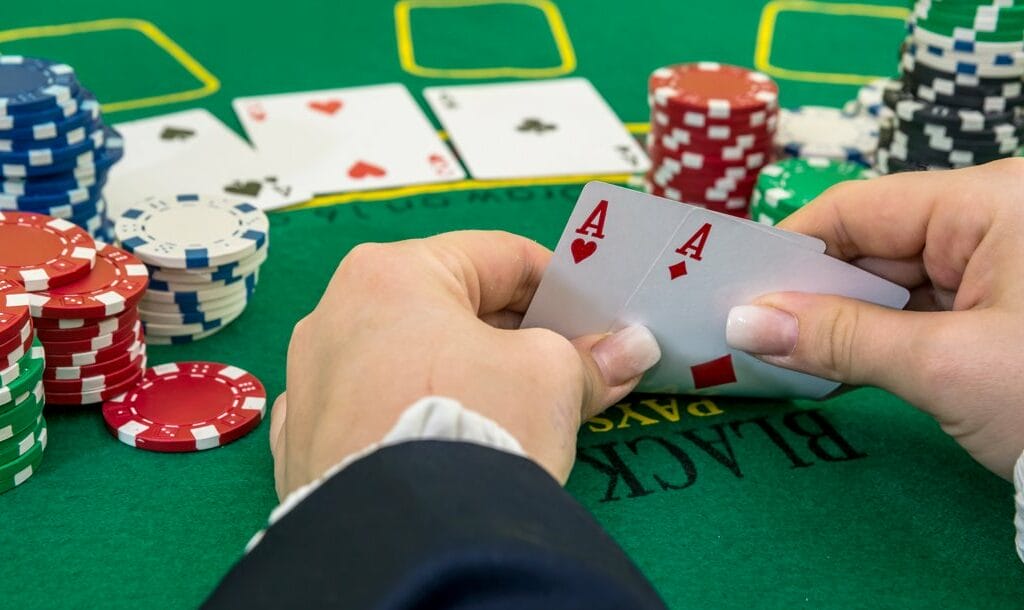A poker player checks their hole cards. They have a pair of aces. They also have multiple stacks of poker chips on either side of their hands.
