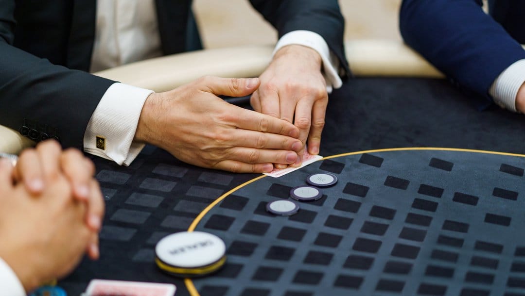 A poker player at a black poker table checks their hole cards. They only have three poker chips left.