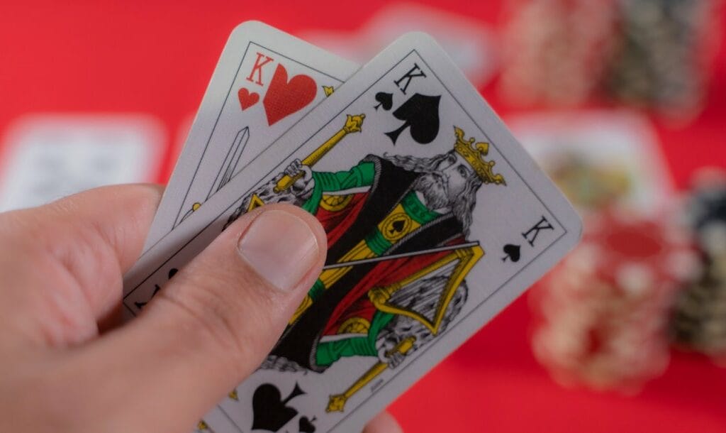 A hand holding two playing cards with a red felt table in the background.