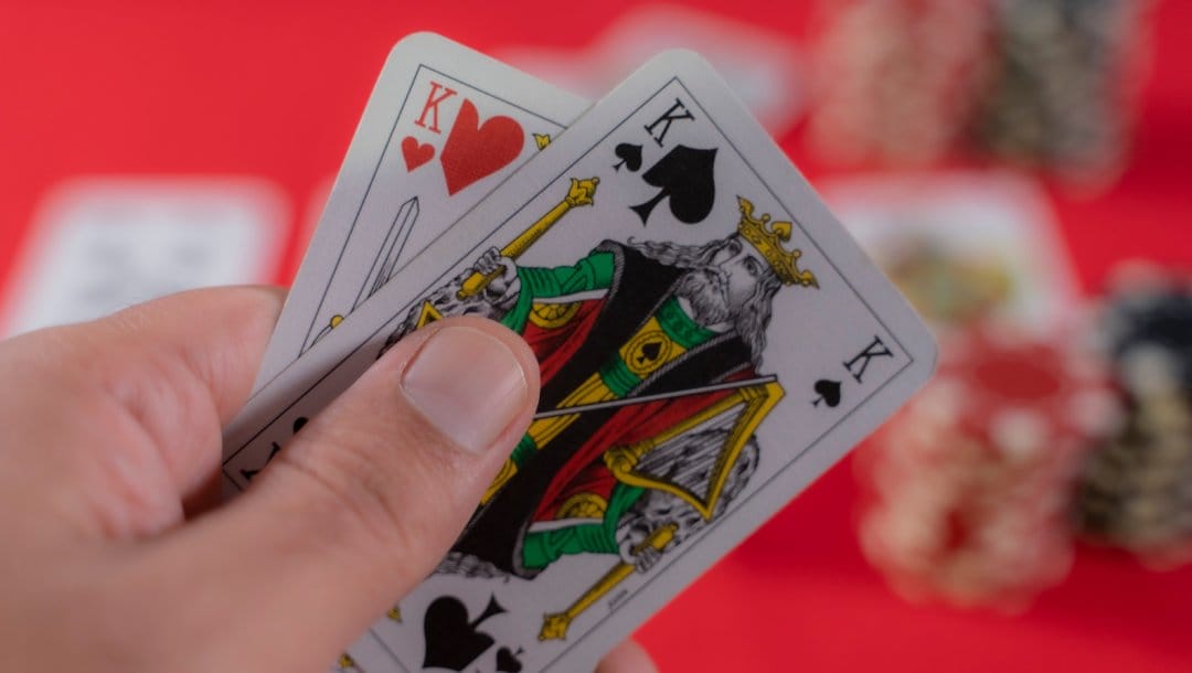 A hand holding two playing cards with a red felt table in the background.