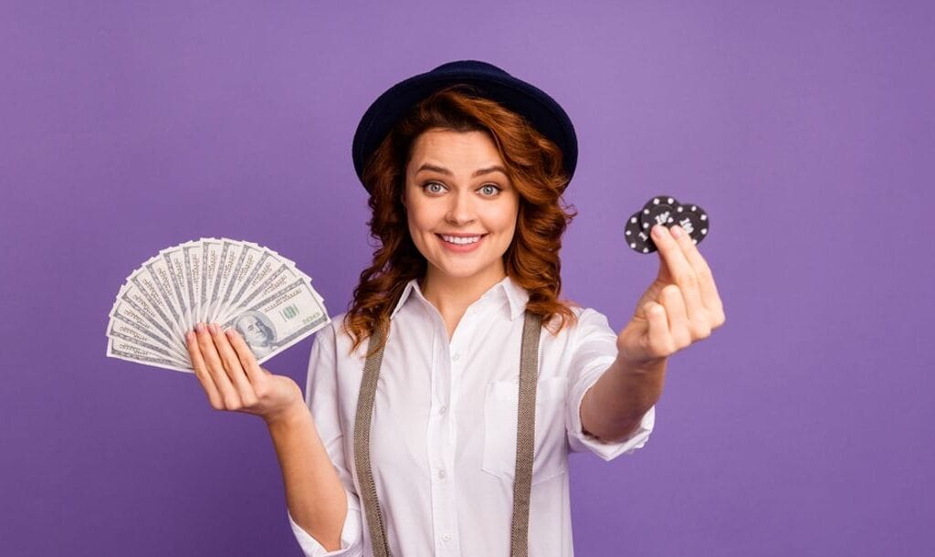 A woman wearing suspenders and a hat holding up casino chips and dollar bills.