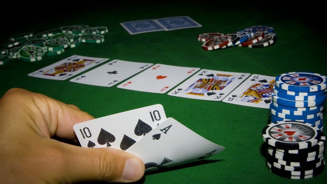 A man holding up a 10 and an ace with casino chips and playing cards on the poker table.