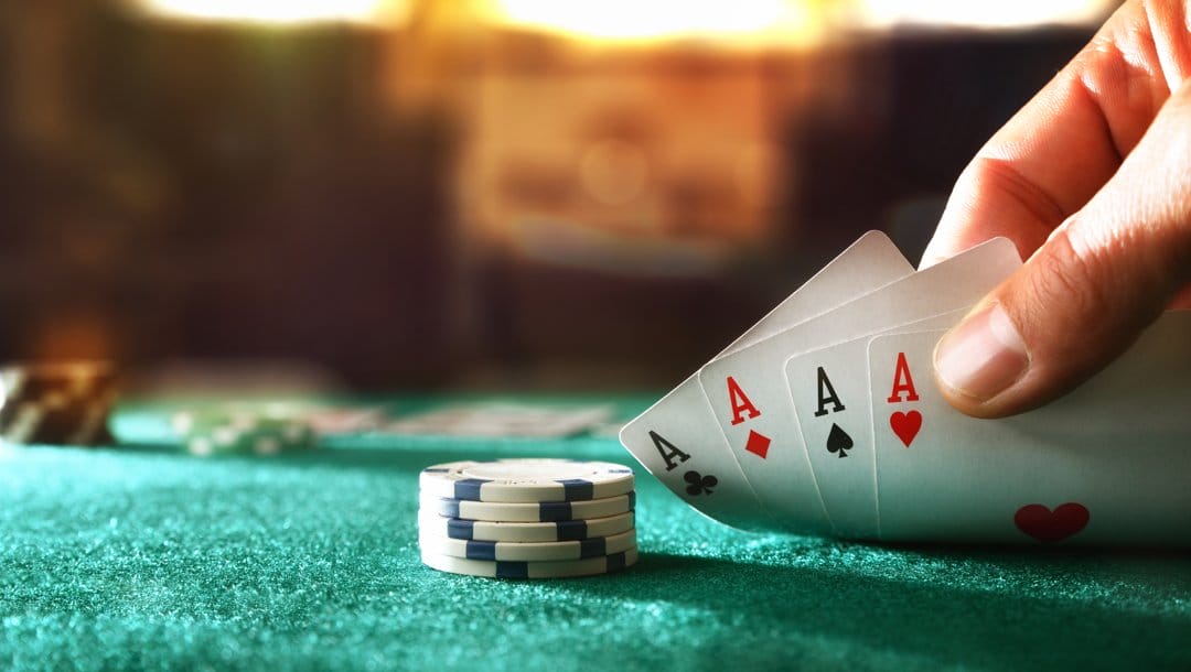 A poker player checks their hole cards. They have four aces.