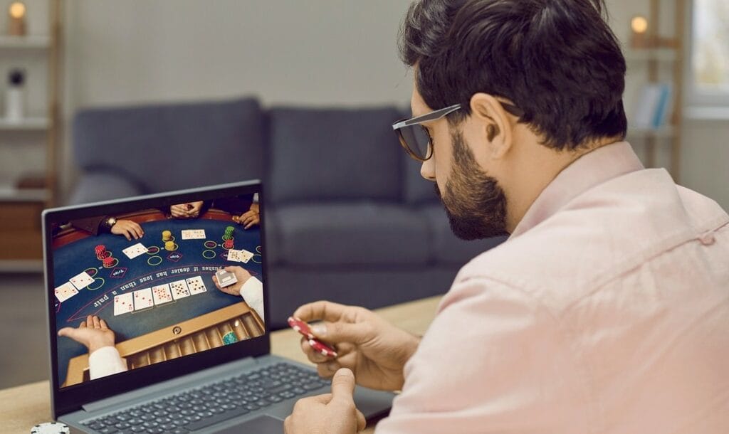 Man sits in front of laptop with poker chips playing online poker.