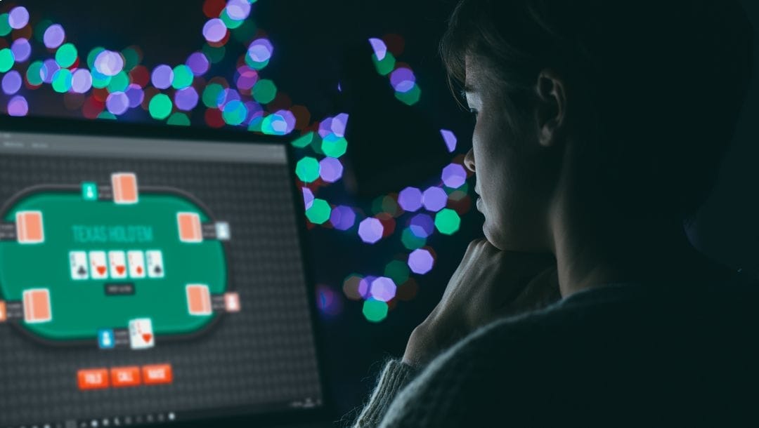 Woman playing online poker on her laptop in a darkly lit room.