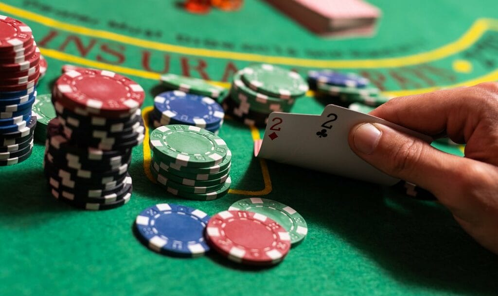 A poker player checks their cards that are on a casino table with stacks of poker chips. They have a pair of twos.