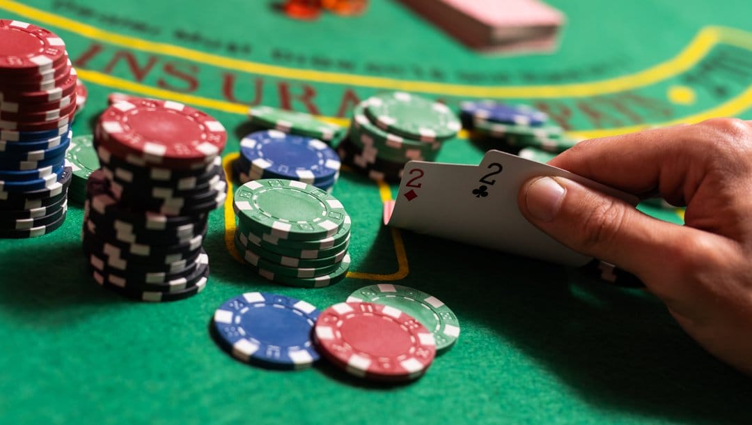 A poker player checks their cards that are on a casino table with stacks of poker chips. They have a pair of twos.