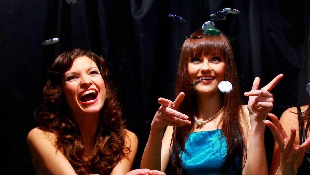 Two people smiling as poker chips fall down onto the table in front of them.