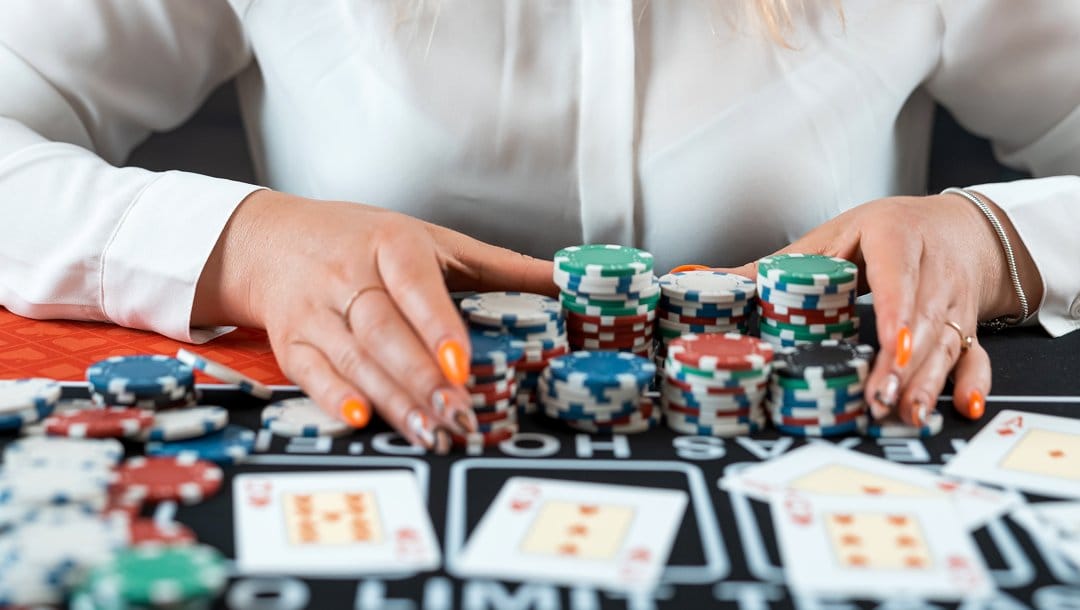 A poker player with their hands around stacks of poker chips. There are some cards and loose chips on the poker table.