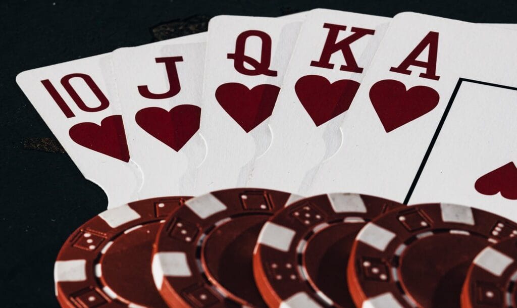 A Royal Flush with five red and white poker chips on top of the cards.