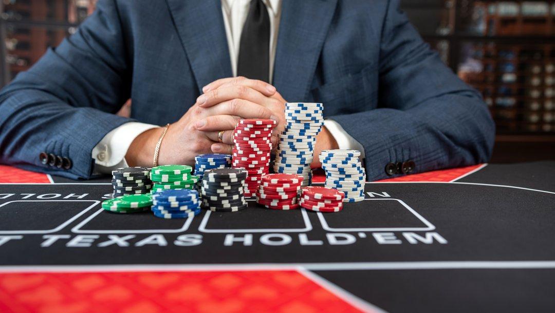 A poker player in a suit with their hands clasped together behind stacks of poker chips.