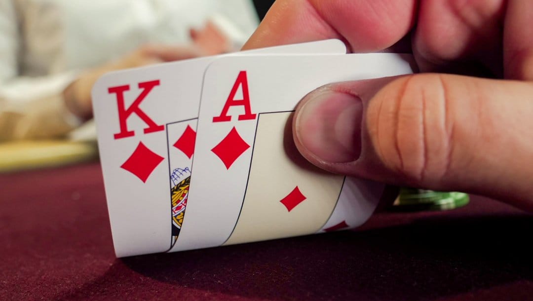 A poker player checks their hole cards — an ace and king of diamonds.