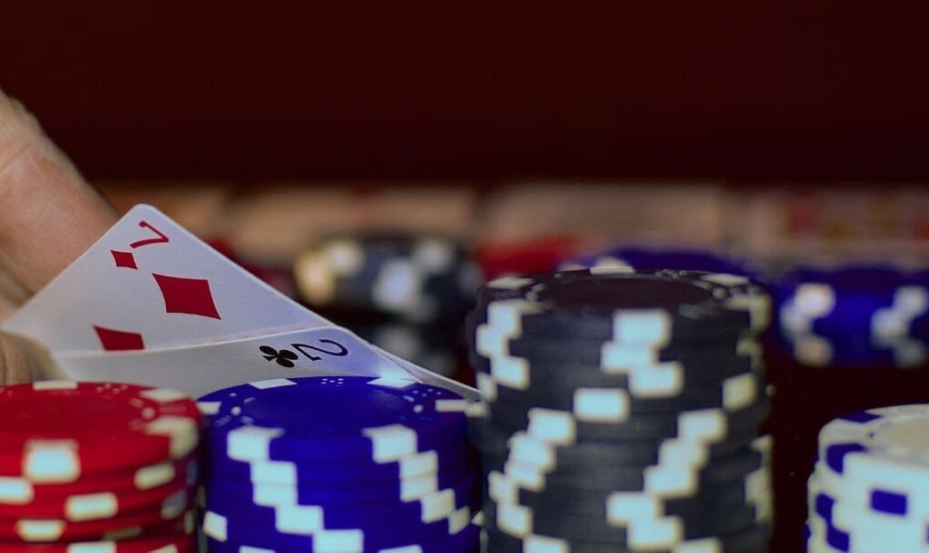 Organized stacks of poker chips by color, hand revealing 7 of diamonds and 2 of clubs in the background.