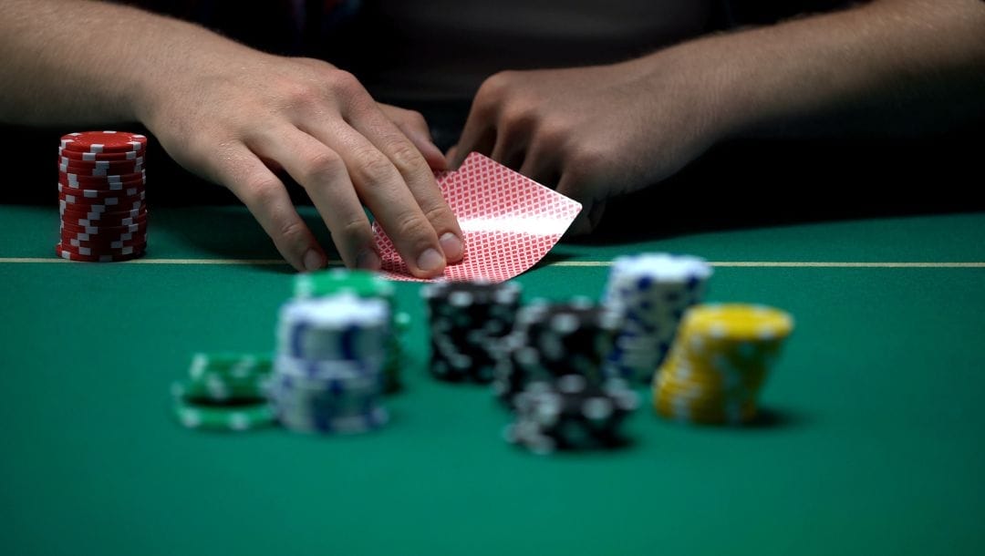 Person closely holding two playing cards, with stacks of chips in front of them.