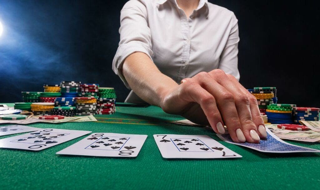 a dealer flips over a playing card on a green felt poker table with poker chips stacked on it