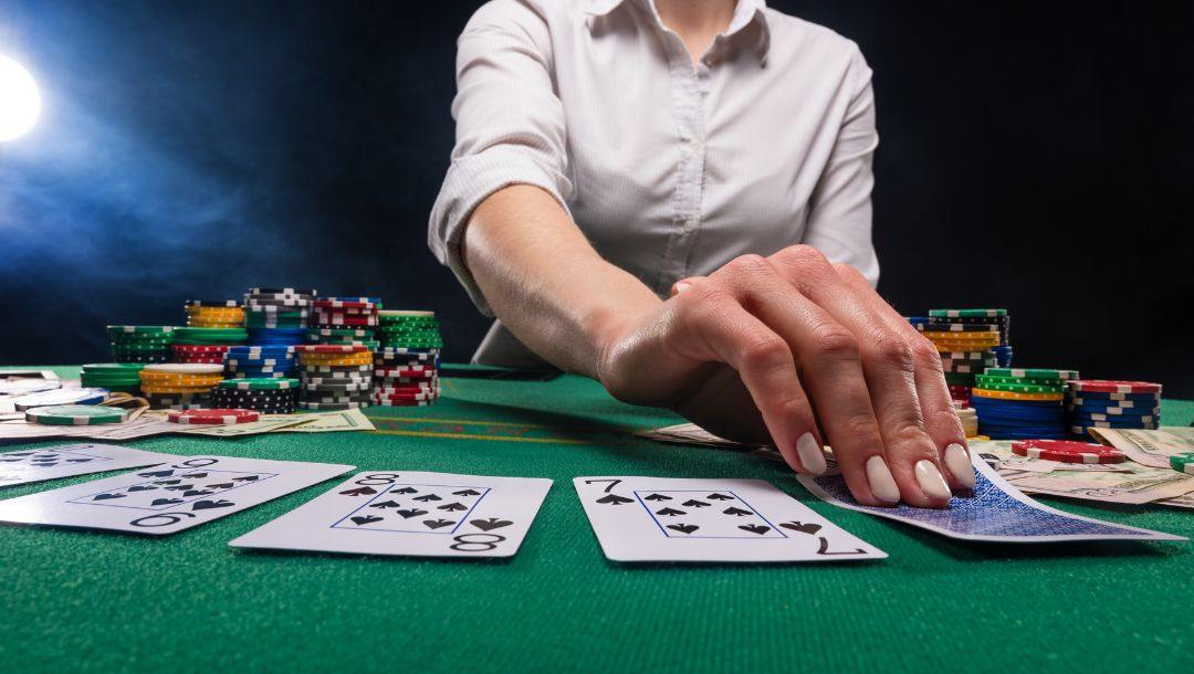 a dealer flips over a playing card on a green felt poker table with poker chips stacked on it